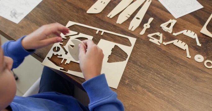 Smart boy hands draw out airplane plywood part of sheet over desk closeup. Schoolboy plays with old aircraft model construction set at home. Creative lesson