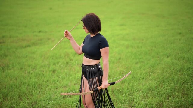 introspective archer woman holding arrow in meadow preparing to nock, casual crop top and fringed skirt with bow at hip intimate profile shots capture steady grip, sunglasses, calm green grass