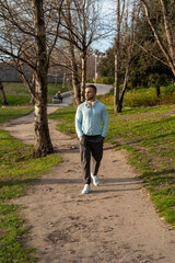 Man walks through a tranquil park path wearing a light blue shirt, enjoying the fresh air and scenic surroundings in the afternoon sun