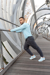 Man stretches on a scenic walkway, enjoying the fresh air and modern architecture early in the morning