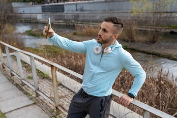 Man in light blue jacket taking a selfie by a serene river while enjoying nature during a sunny daytime