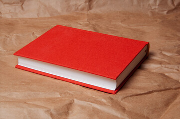 A closed red hardcover book rests on a textured brown paper background