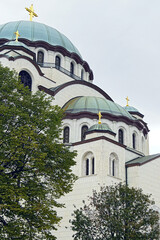 Domes of the Church of Saint Sava rising above trees in Belgrade. Represents orthodox spirituality, Serbian religious heritage, sacred architecture, european faith traditions, and cultural landmark.