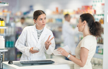 Friendly female pharmacist helping woman with prescription choosing medical supplies at drugstore