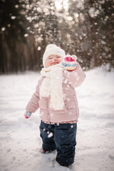 Fototapeta premium Snowfall. Kid enjoying and walking in a snowy forest. Happy family holidays. Little girl standing in winter park. Portrait of a cute child having fun and playing with snow. Frosty winter season.