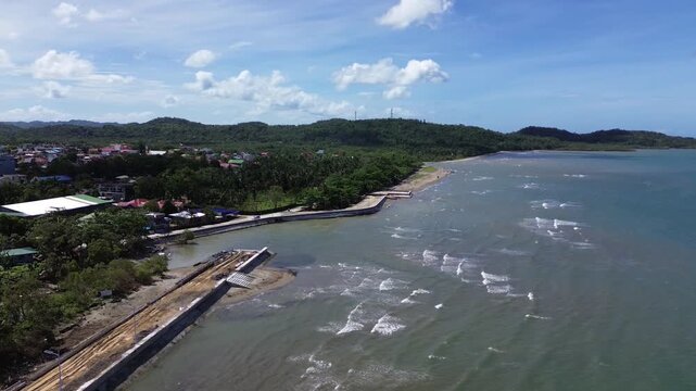 Aerial drone footage of the coastal seawall in Odiongan City on Tablas Island, Philippines, showing a concrete beachfront promenade with palm-lined shoreline, blue sea, and hills in the background.