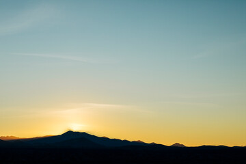Naklejka premium Sun setting behind silhouetted mountain landscape