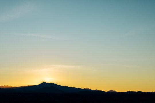 Sun setting behind silhouetted mountain landscape