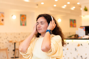 Young woman wearing headphones working with laptop in modern city cafe