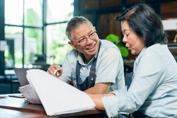 Obraz premium Elderly asian couple wearing apron smiling while reviewing document together at wooden table in restaurant discussing small business planning teamwork cooperation partnership expressing positive work