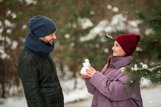 teenage daughter shows father small snowman in winter park.