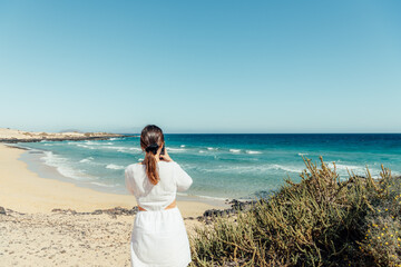Young woman photographing the ocean on a sunny beach day in summer