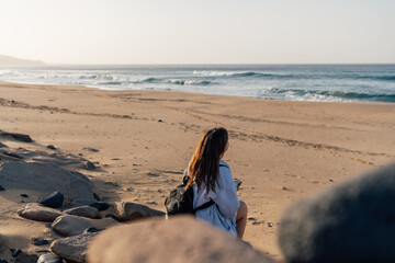 Young Caucasian woman sitting on Cofete beach looking at the ocean