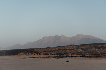 Vehicles parked near volcanic mountains in Cofete