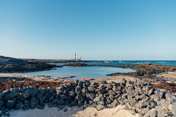 Volcanic stone wall and coastal view of El Tost&oacute;n lighthouse