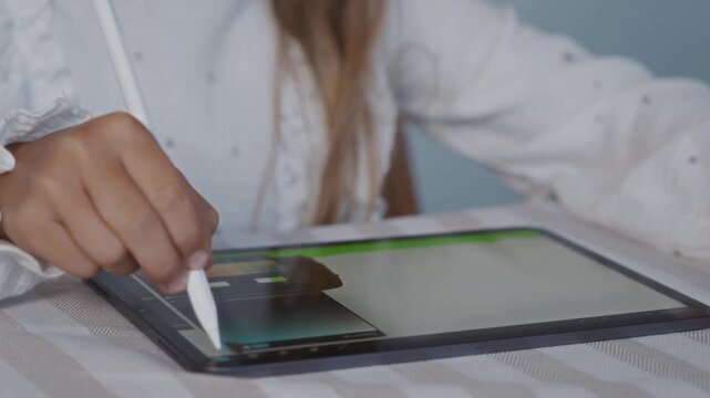 Close up shot from a slight top front angle shows a child interacting with a drawing application on a digital tablet using a stylus. The camera captures focused learning and digital creativity. 4k