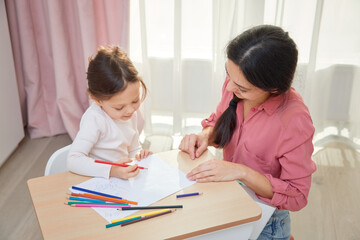 Mother and cute little daughter drawing with colored pencils, engaging in creative home learning
