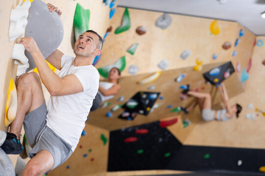 Male visitor to fitness club clambs wall for amateur climbers, side view. Active recreation, hobbies, recreation for active and sporty people