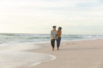 Full length of happy couple walking together on shore at beach against sky during sunset