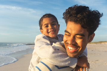 Close-up of happy father giving son piggyback ride to son at beach against sky