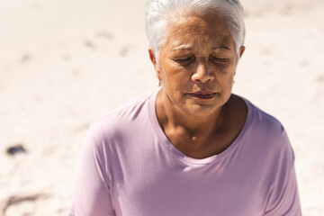 senior woman meditating with eyes closed at beach on sunny day