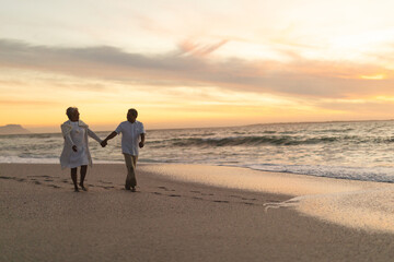 Senior couple holds hands on beach walk at sunset