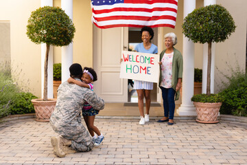 Smiling african american women looking at girl embracing father soldier's return home at entrance