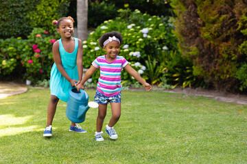 Two african american sisters with watering can running in garden