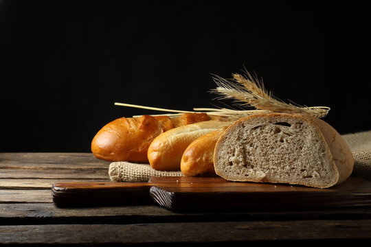 Freshly baked assorted bread loaves, buns, and wheat ears on a rustic wooden table - Powered by Adobe