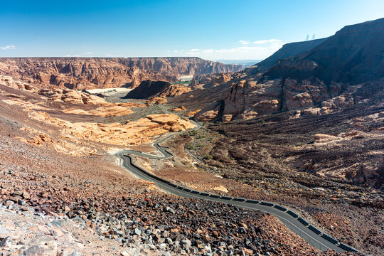 Saudi Arabia, winding desert canyon road through rugged red rock landscape under clear blue sky - Powered by Adobe