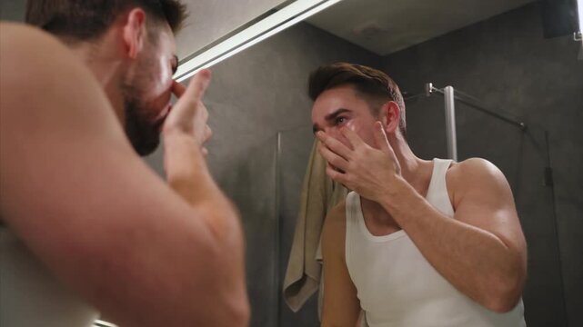Man applying under eye patches in front of a bathroom mirror