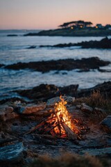 Fototapeta premium A campfire on a rocky beach at dusk, with waves nearby and distant lights on the shoreline. Concept Rocky beach campfire at dusk, Distant shoreline lights, Waves crashing at twilight