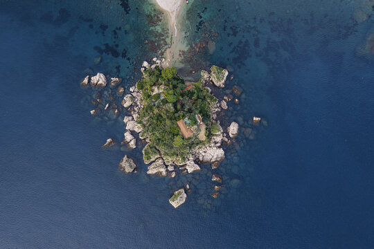 Aerial view of Isola Bella, a jewel of an island crowned with lush greenery and rocky shores, connected by a sandy isthmus to the mainland, Taormina, Sicily, Italy.