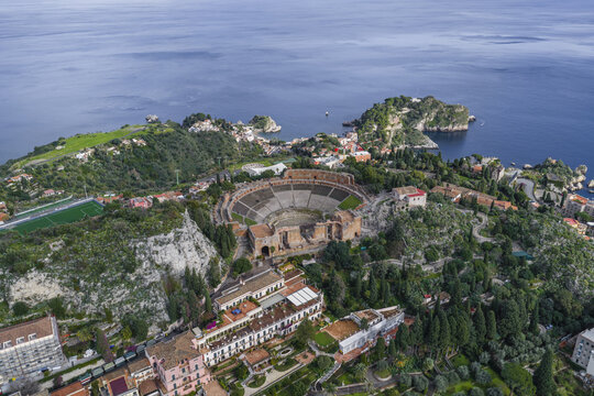 Aerial view of the ancient Teatro Antico standing majestically against the deep blue of the Ionian Sea, its weathered stones echoing centuries of history, Taormina, Sicily, Italy.