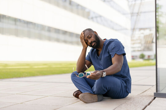 Healthcare worker sitting on the floor outdoors looking stressed and tired
