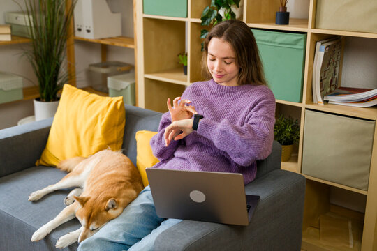 Woman relaxing with pet and checking smartwatch in cozy living room
