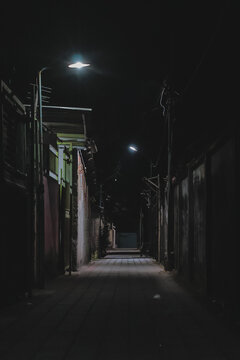 Dimly lit alleyway at night with streetlights creating a mysterious atmosphere and copy space, ideal for urban thrillers and suspenseful narratives