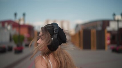 young white woman hairflip with headphones on city avenue, turning and tossing long hair while smiling at camera back shots and front smiles alternate, motion blur and breeze emphasize dynamic