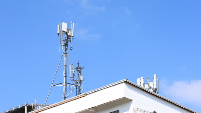 Cell tower on the roof of a building. Macro base station or base transmitter, telecommunications station with antennas of 4G and 5G cellular against blue background. Selective focus
