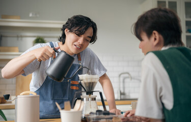 Asian gay couple making fresh pour-over coffee together in home kitchen. A warm domestic lifestyle moment showing a romantic morning routine, brewing caffeine, and bonding with love