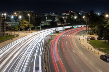 Obraz premium Night city traffic captured with long exposure showing dynamic light trails on a wide urban road in Athens, Greece. Modern transport, motion, speed and city life concept.