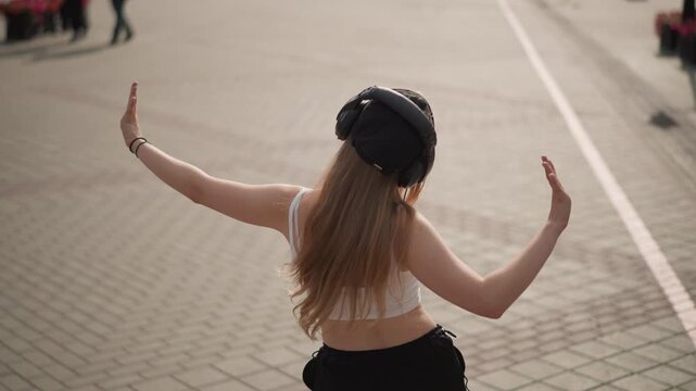 urban street dancer wearing wired headphones, moving across tiled plaza with rhythmic arms and turns casual crop top and trousers, backtocamera moments shift to direct gaze, warm pavement tones,
