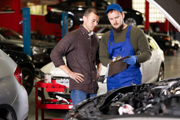 Young male mechanic signs agreement with young male client of car service center