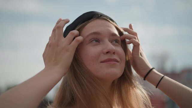 young woman adjusting beanie on street, soft backlight, wistful expression, long hair moved by breeze, freckled skin, shallow depth, brick urban background, cinematic colorgrade, slow motion broll