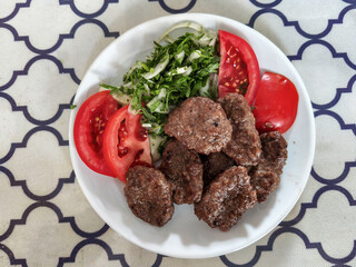 Mugla - Milas district: Meatballs, tomatoes, and onions served on a white plate.