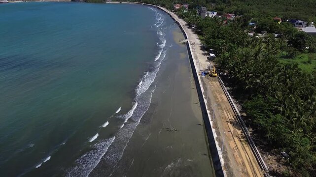 Aerial drone footage of the coastal seawall in Odiongan City on Tablas Island, Philippines, showing a concrete beachfront promenade with palm-lined shoreline, blue sea, and hills in the background.