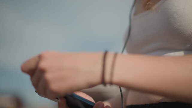 Woman tests music, Girl connects headphones while enjoying relaxed summer street dance practice, Young woman outdoors tests her music setup for casual summer street dance training session