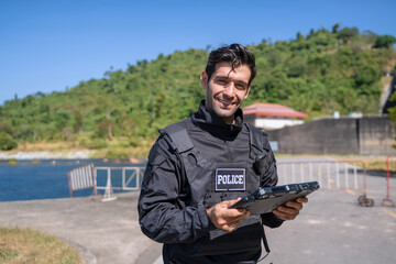 The police officer is working with rugged laptop at the dam.