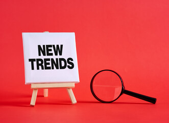Magnifying glass exploring new trends written on canvas on red background