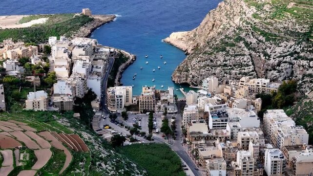 High angle aerial view of Xlendi Bay Gozo Malta during a bright sunny summer day featuring turquoise Mediterranean waters surrounded by limestone cliffs and white buildings nestled in the green valley